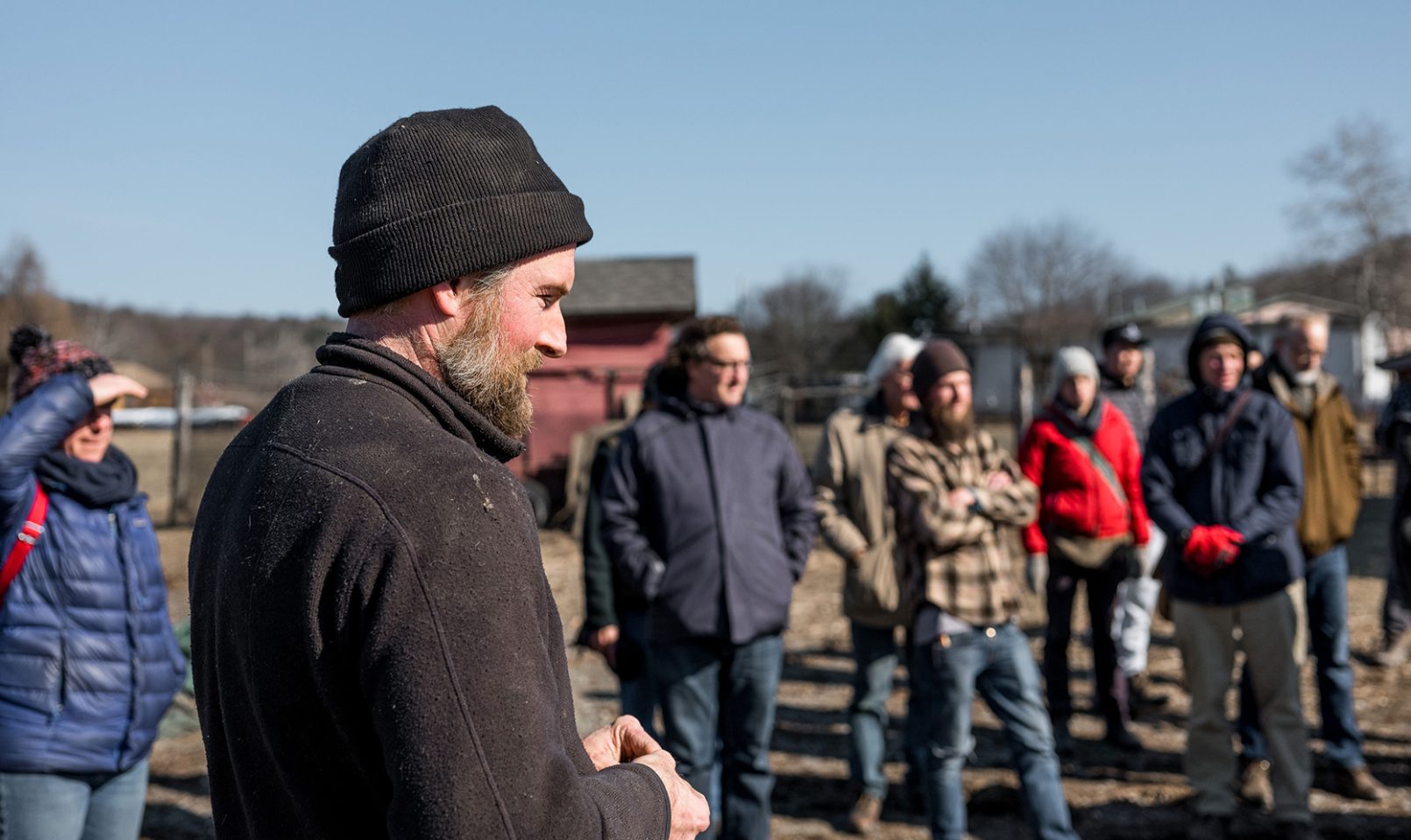 focus on Spencer Fenniman, farm manager, as he stands outside with a group of people giving the IMA soil demonstration