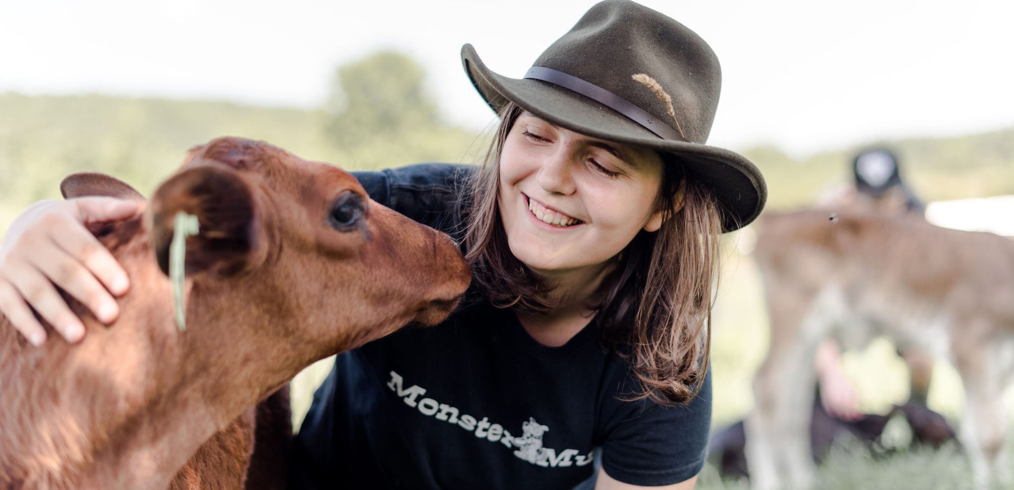 A summer camp student smiling, looking at a calf with a hand on the calf's neck