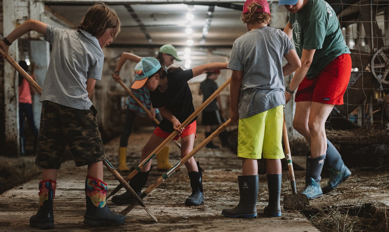farm camp students in the milking barn with a counselor scraping mud off the ground