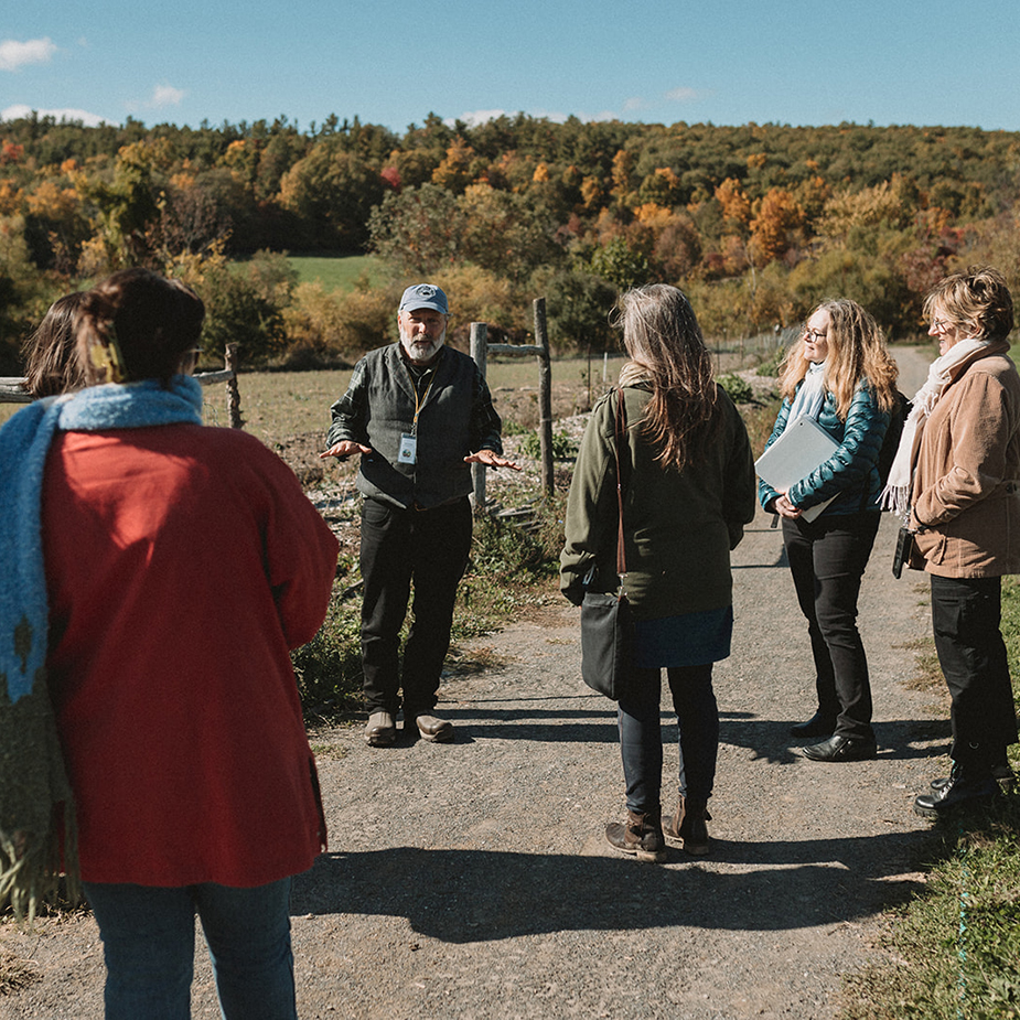 Martin Ping talking to a group of people while out on a trail, the fall foliage in the background